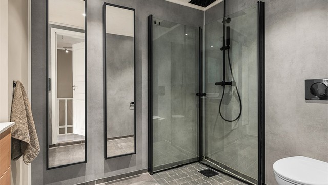 Videre er badet innredet med servantskap med speil, vegghengt toalett og dusjhjørne med regndusj.