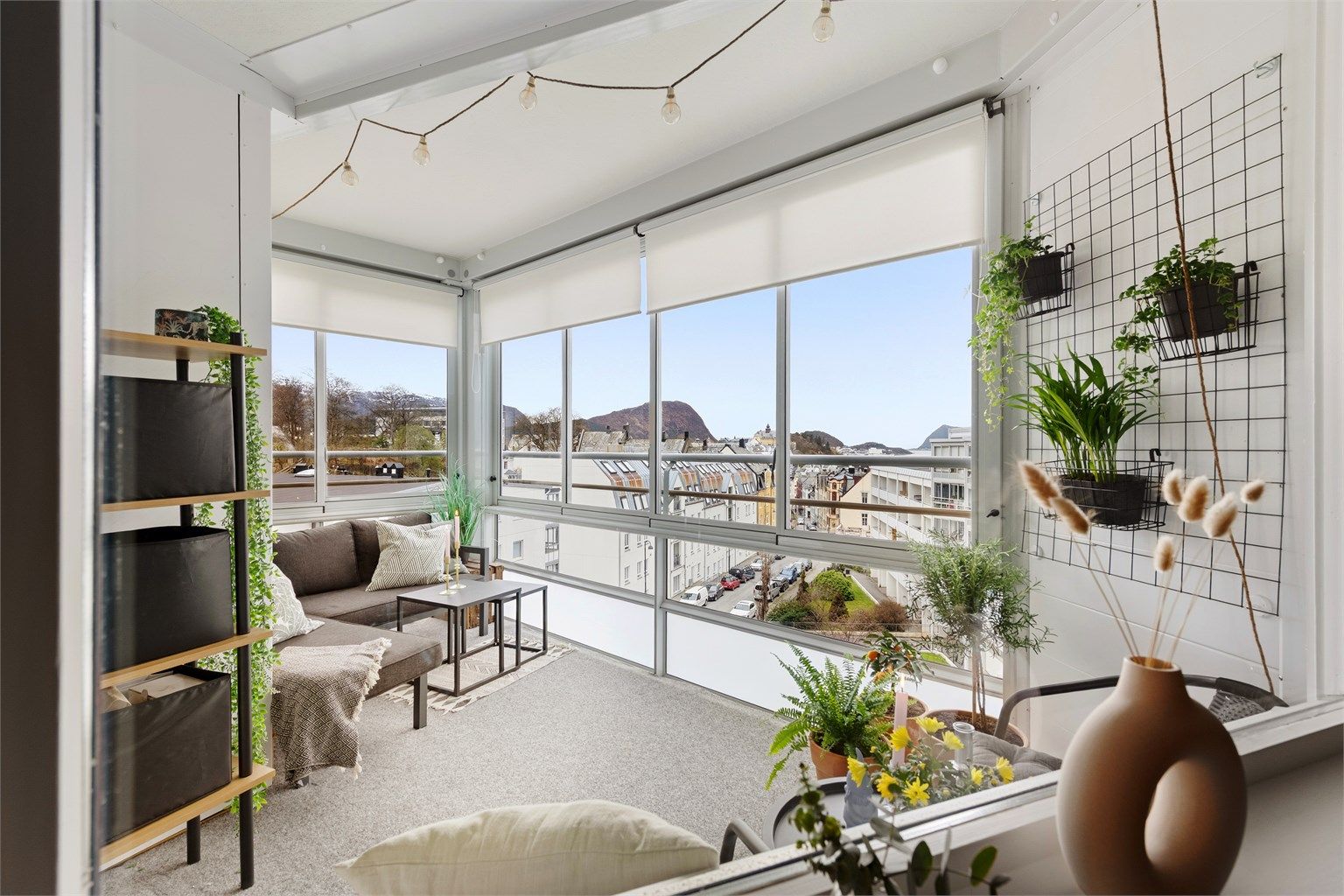 Inneglasset balkong med vegg til vegg tepper på gulv. Persienner i vindu. Flott vestvendt utsikt mot bysentrum