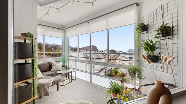 Inneglasset balkong med vegg til vegg tepper på gulv. Persienner i vindu. Flott vestvendt utsikt mot bysentrum