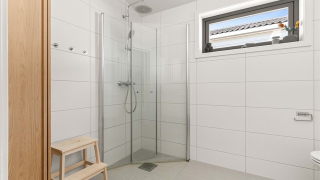 Badet er utstyrt med dusjhjørne, vegghengt toalett og servantinnredning.
