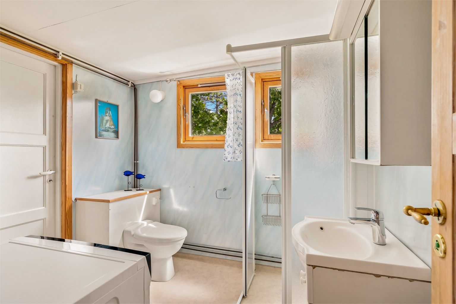 Enkelt bad med wc, servant i seksjon, dusjhjørne og opplegg til vaskemaskin. Fra badet er det også utgang.