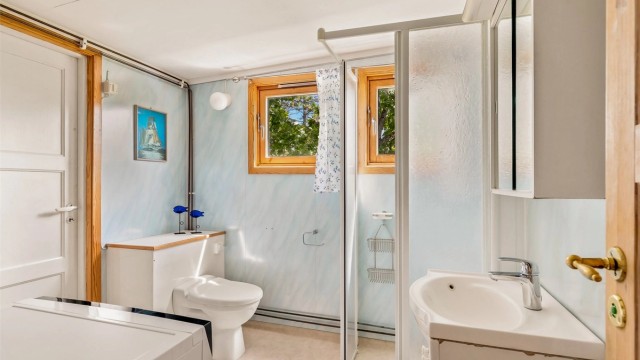 Enkelt bad med wc, servant i seksjon, dusjhjørne og opplegg til vaskemaskin. Fra badet er det også utgang.
