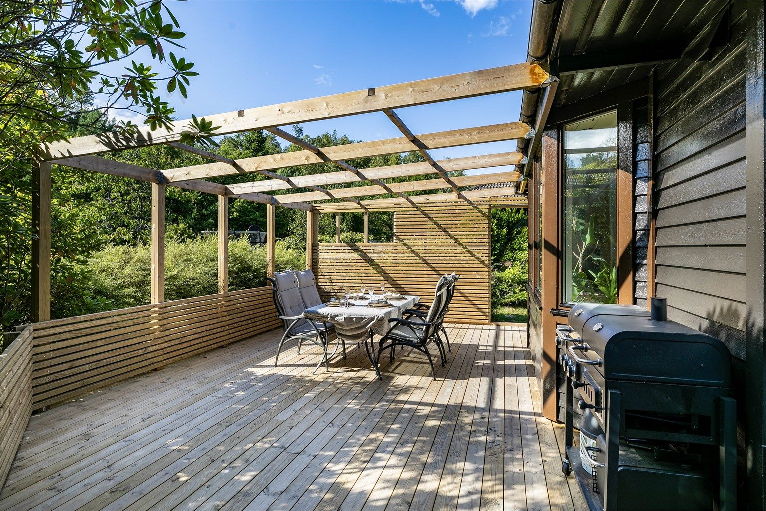 På den store terrassen er det god plass til grilling og sammenkomster utendørs. Spilevegger og hagens beplantning ivaretar privatlivet.