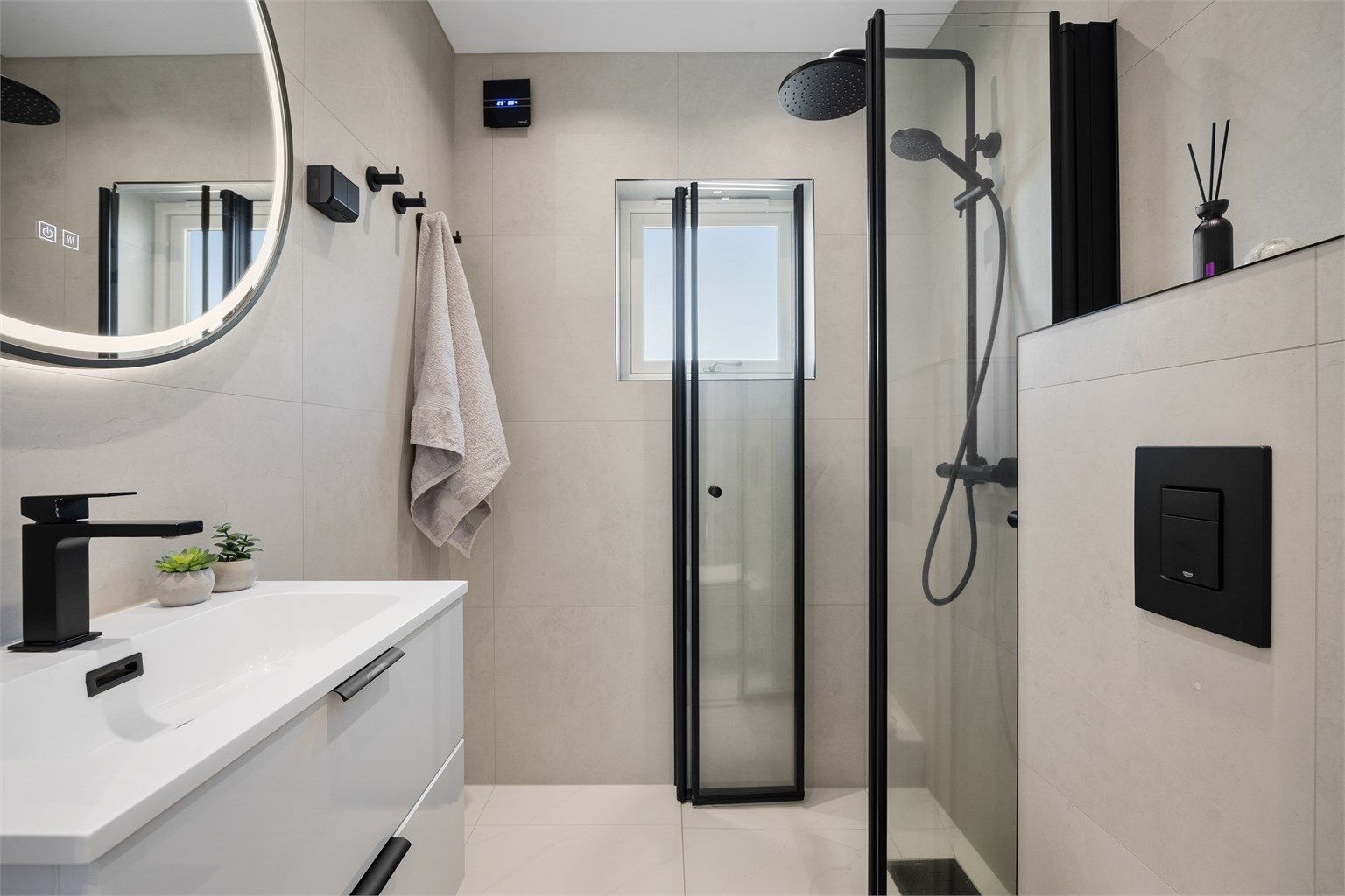 Pent og lyst flislagt baderom med svarte detaljer 