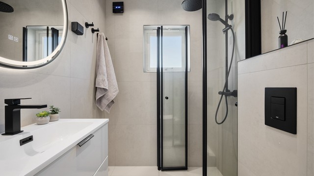 Pent og lyst flislagt baderom med svarte detaljer