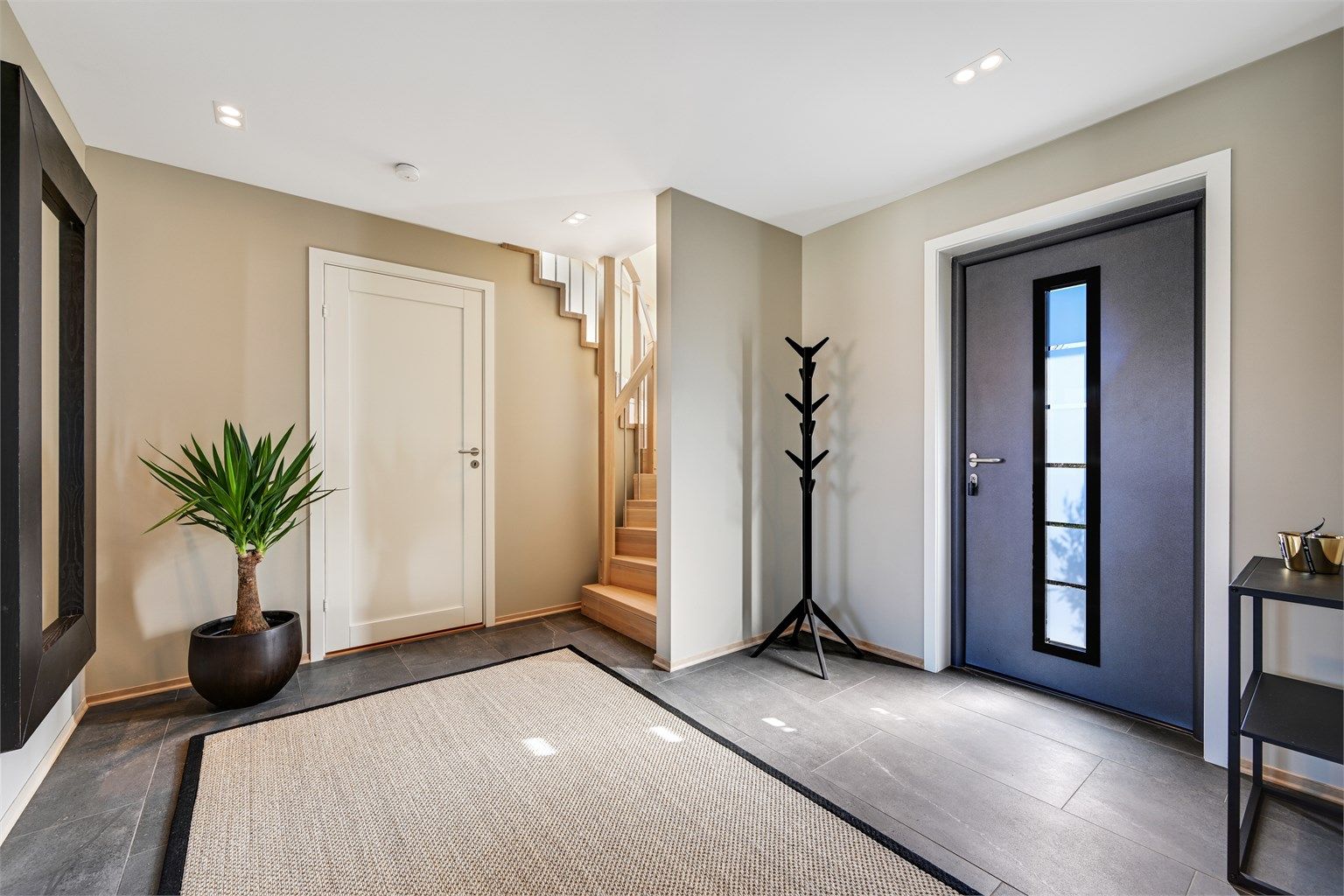 Romslig hall med flislagt gulv. Herfra leder en heltre eiketrapp opp til andre etasje.