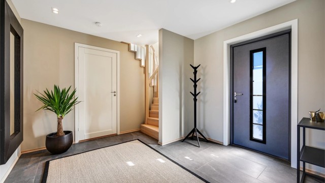 Romslig hall med flislagt gulv. Herfra leder en heltre eiketrapp opp til andre etasje.