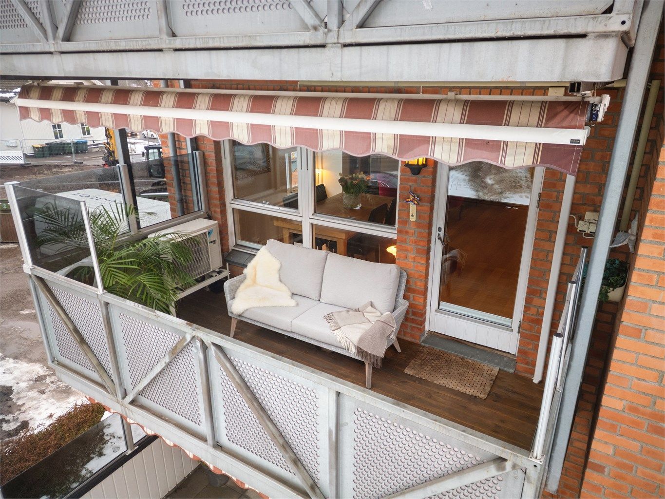 Balkongen er utstyrt med levegger av glass på rekkverk, utvendig belysning, strømuttak, markise, terrassevarmer og terrassebord på gulv.