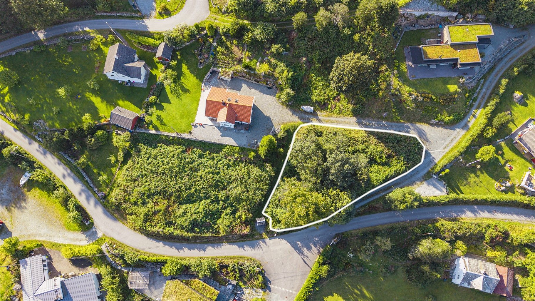 Tomten ligger i grønne omgivelser med etablert bebyggelse og adkomstvei rett ved tomtegrensen.