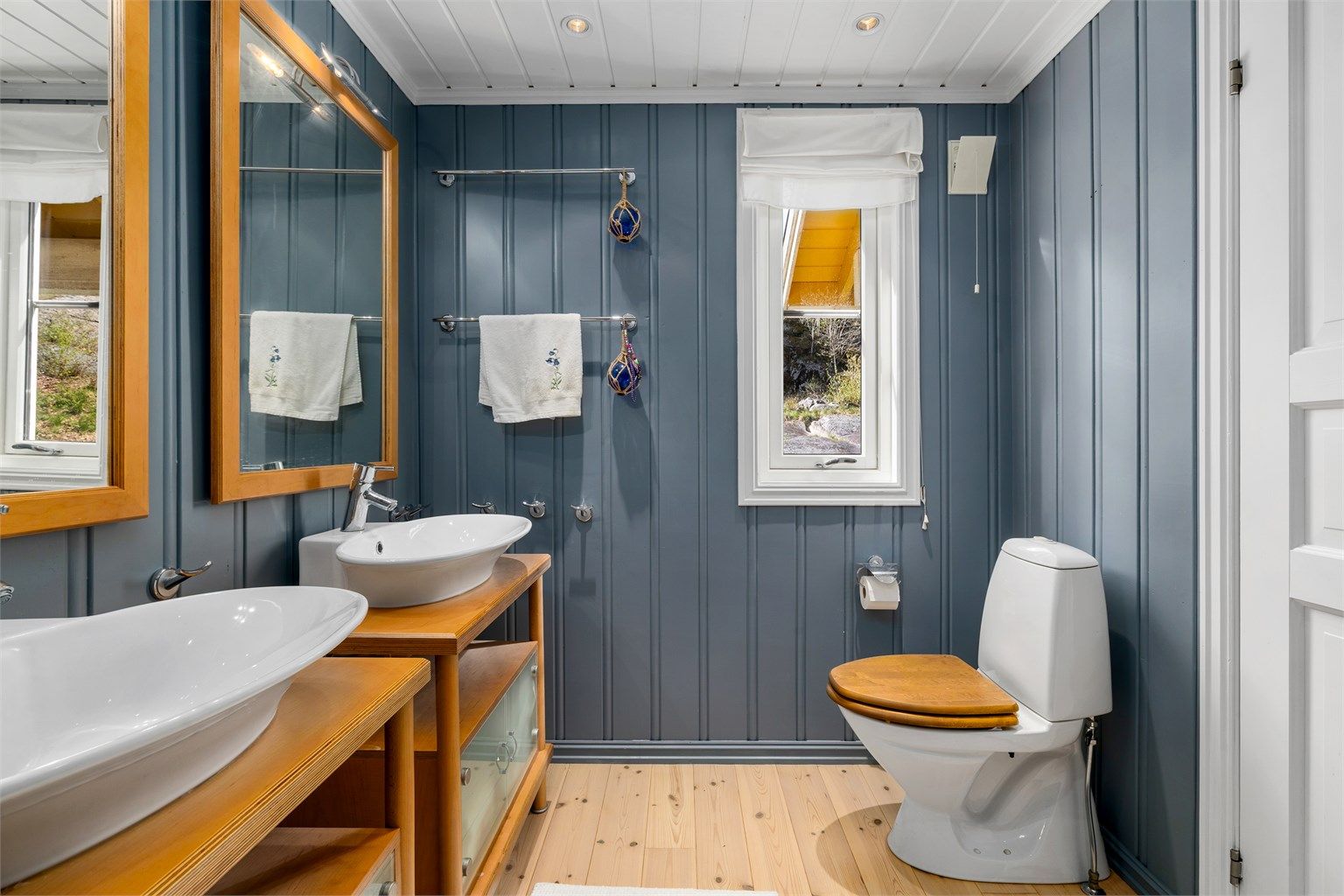 Lyst og romslig bad i 1. etasje med malte overflater og klassisk tregulv. Rommet er smakfullt innredet med to servanter med store speil, høyskap, og møblet er i solid heltre. Dusjkabinett og toalett er montert.