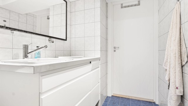 Lyst og romslig helfliset bad med opplegg for vaskemaskin.