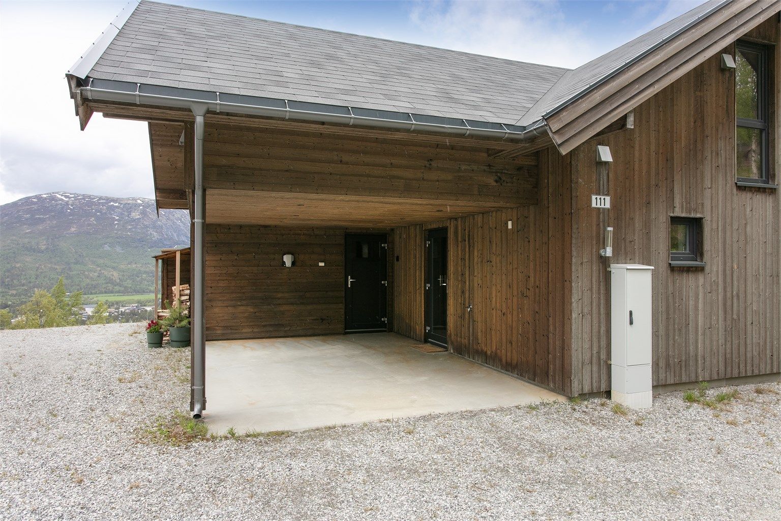 Praktisk carport med direkte adkomst til inngangspartiet og integrert vedoppbevaring.