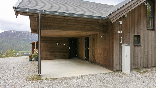 Praktisk carport med direkte adkomst til inngangspartiet og integrert vedoppbevaring.