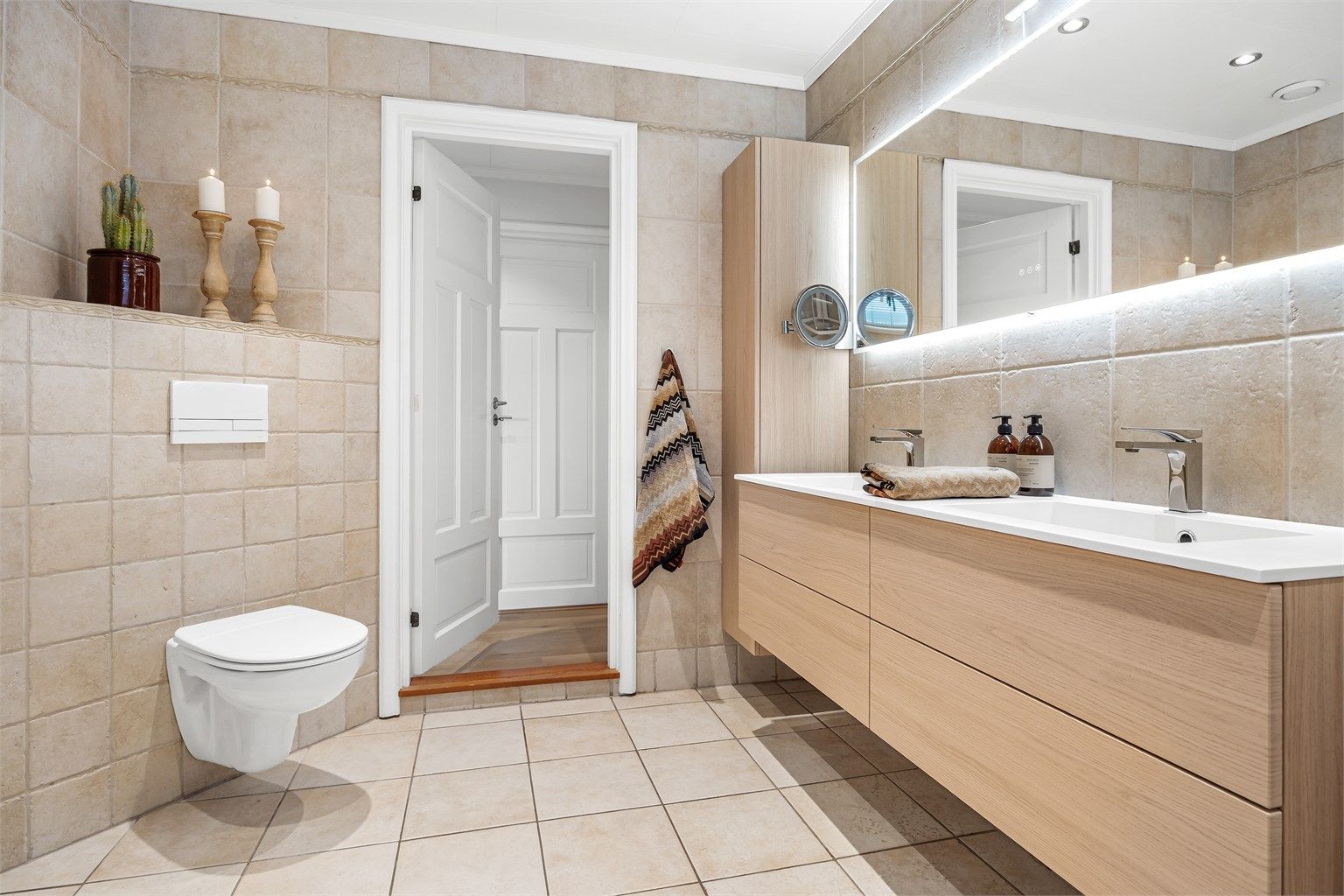 Romslig baderomsinnredning med heldekkende dobbelservant, vegghengte høyskap og speil med integrert lys.