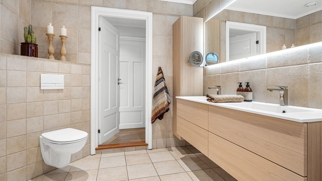 Romslig baderomsinnredning med heldekkende dobbelservant, vegghengte høyskap og speil med integrert lys.