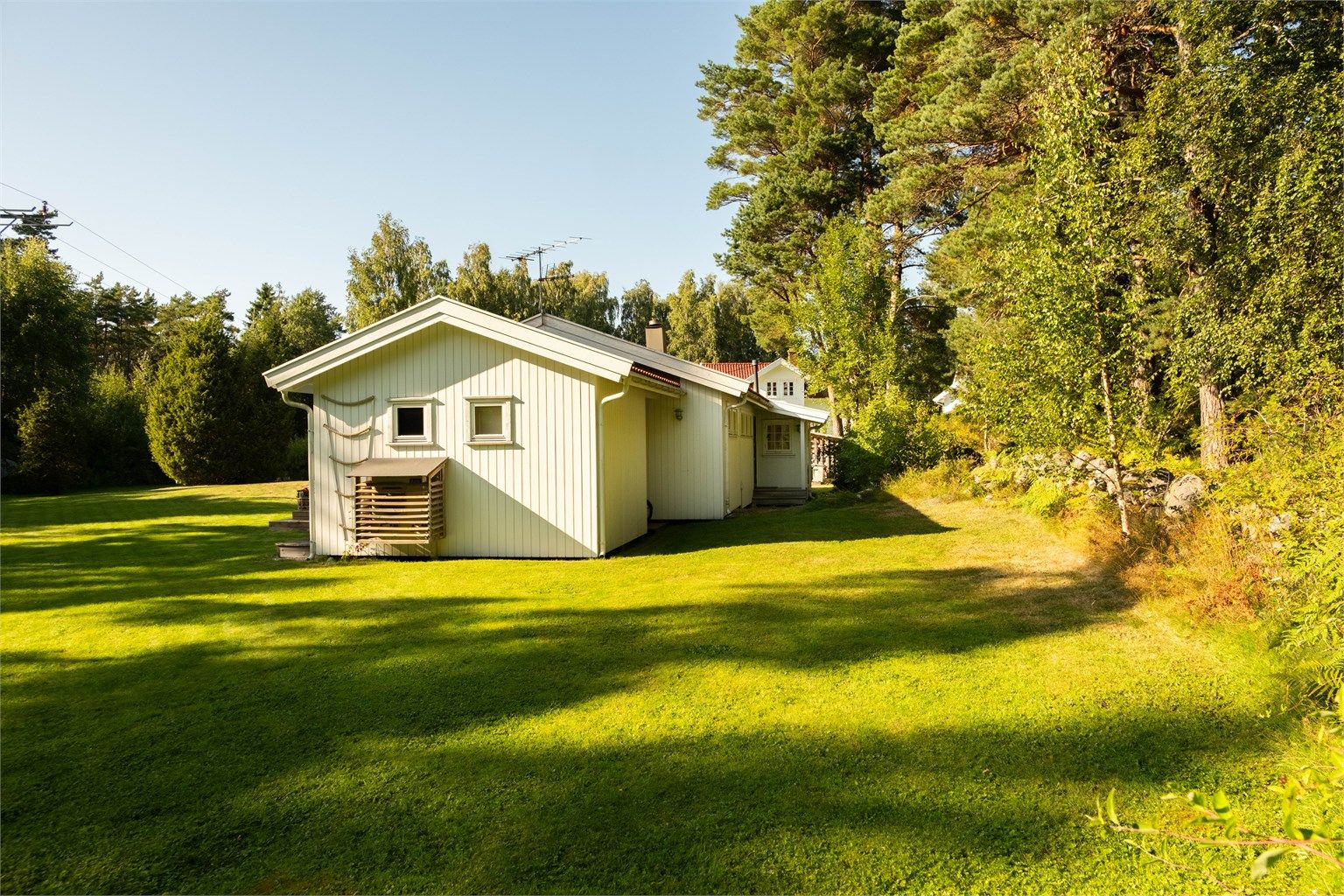 Steingjerde og naturlig vegetasjon avgrenser hagen mot Gjøkvikveien som følger østre tomtegrense.