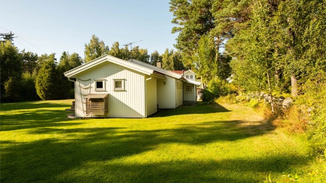 Steingjerde og naturlig vegetasjon avgrenser hagen mot Gjøkvikveien som følger østre tomtegrense.