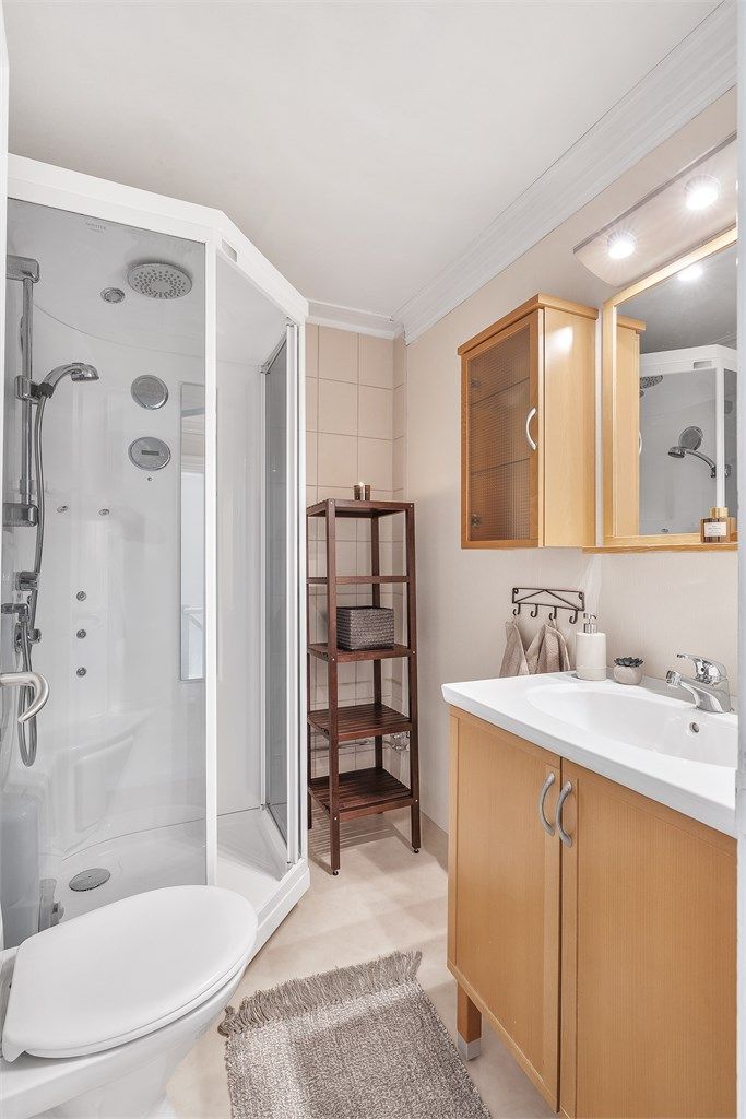 Bad i 2.etg med belegg på gulv og fliser/tapet på vegg. Malte himlingsflater. Innredet med dusjkabinett, toalett, gulvstående servant, speil med overlys