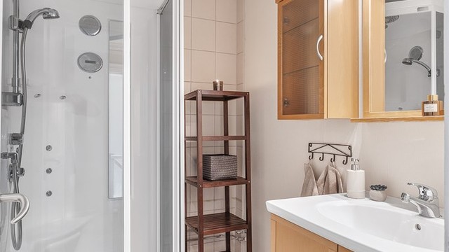 Bad i 2.etg med belegg på gulv og fliser/tapet på vegg. Malte himlingsflater. Innredet med dusjkabinett, toalett, gulvstående servant, speil med overlys