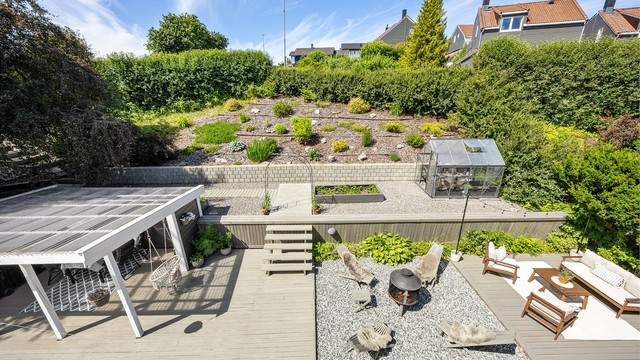 Oversikt over det flotte uteområdet med drivhus, plen og stor terrasse.