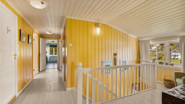 Gang i andre etasje med malt tretrapp og panel på vegger.