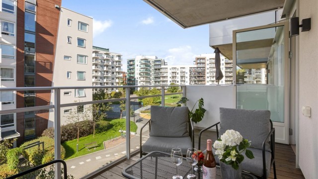 Vestvendt uteplass med utsikt over gårdstun. Gulv med terrassebord. Rekkverk i stål med innfelte glassplater. Belysning og stikkontakter.