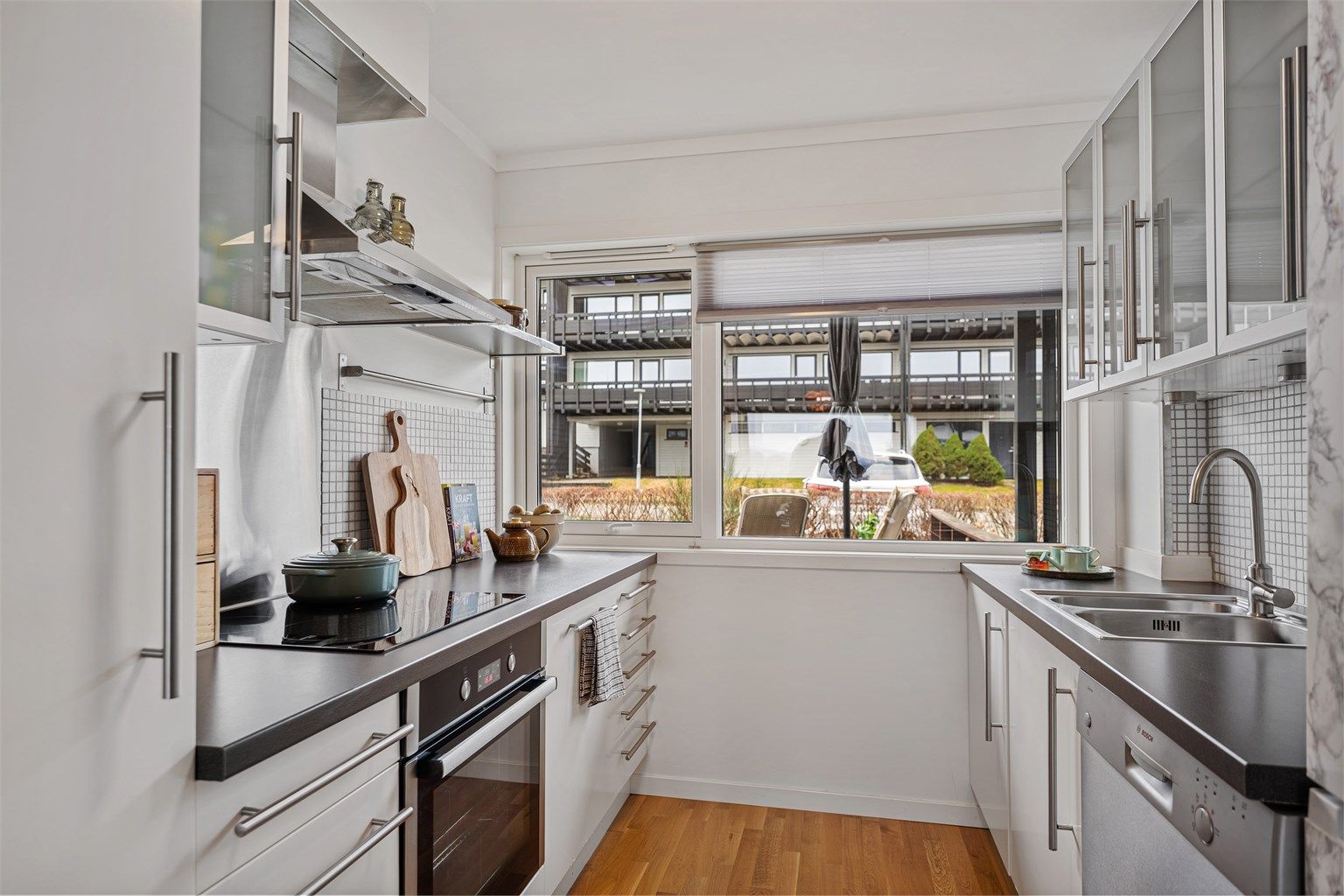 Kjøkkeninnredningen fra IKEA i tidløs hvit og grå benkeplate. Fliser på vegg mellom overskap og benk, i tillegg til stort vindu på endevegg, som gir godt lysinnslipp og utsikt mot inngangsparti og den sør-vendte terrassen. 