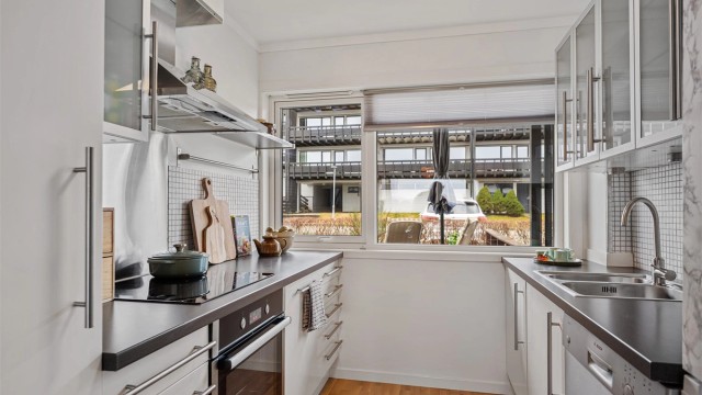 Kjøkkeninnredningen fra IKEA i tidløs hvit og grå benkeplate. Fliser på vegg mellom overskap og benk, i tillegg til stort vindu på endevegg, som gir godt lysinnslipp og utsikt mot inngangsparti og den sør-vendte terrassen.