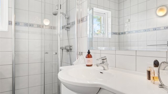 Flislagt bad med gulvvarme. Innredningen inkluderer servant med underskap og dusjhjørne med innfellbare glassdører.