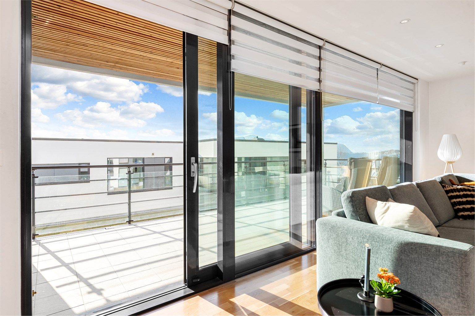 Utgang fra stue via skyvedør til overbygd terrasse med rekkverk i stål og glass