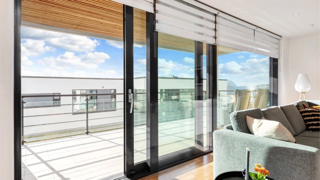 Utgang fra stue via skyvedør til overbygd terrasse med rekkverk i stål og glass