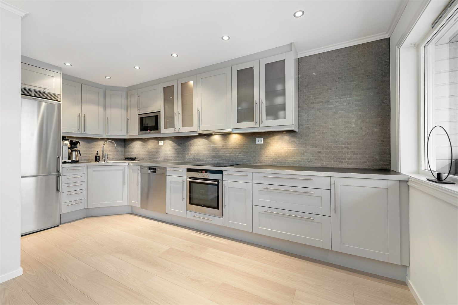 Kjøkkeninnredningen er fra Norema og har grå profilerte fronter og benkeplate av laminat med nedfelt oppvaskkum med ett-greps kjøkkenarmatur. 