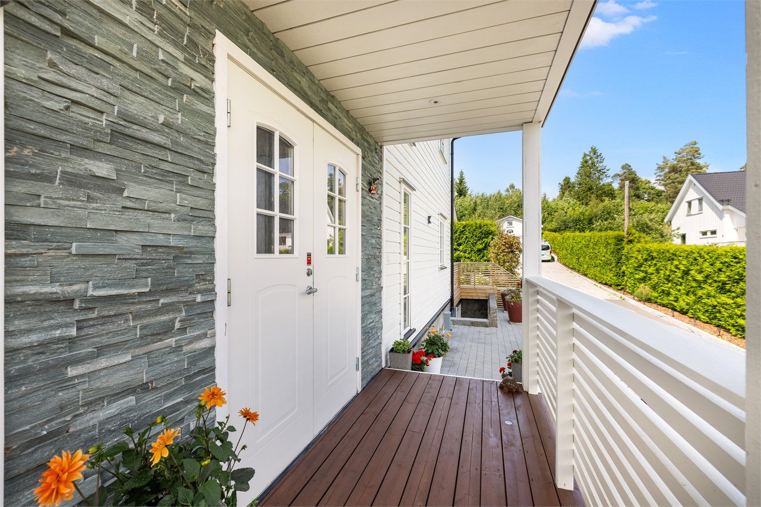 Et pent og overbygget inngangsparti med steinpanel rundt inngangsdøren og innfelte downlights i himlingen.