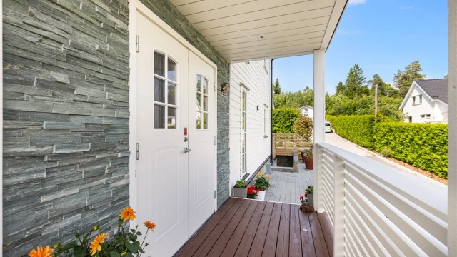 Et pent og overbygget inngangsparti med steinpanel rundt inngangsdøren og innfelte downlights i himlingen.