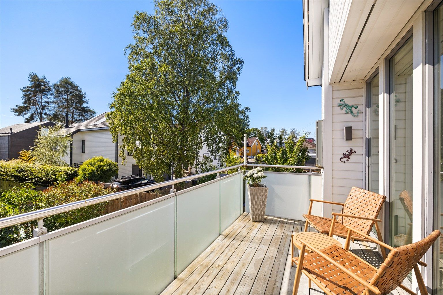 Balkongen har terrassebord på gulvet og et rekkverk i metall og glass.