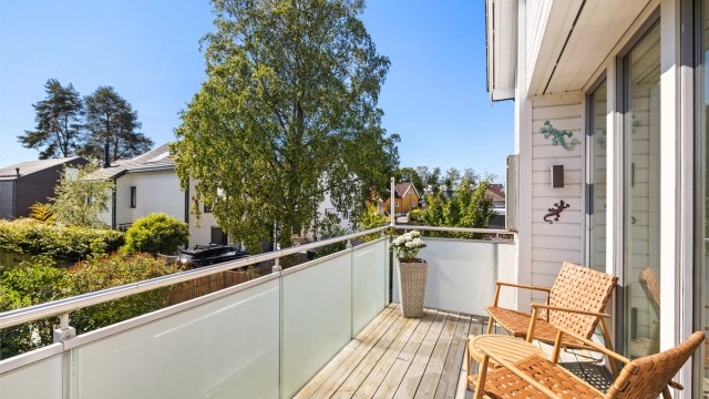 Balkongen har terrassebord på gulvet og et rekkverk i metall og glass.