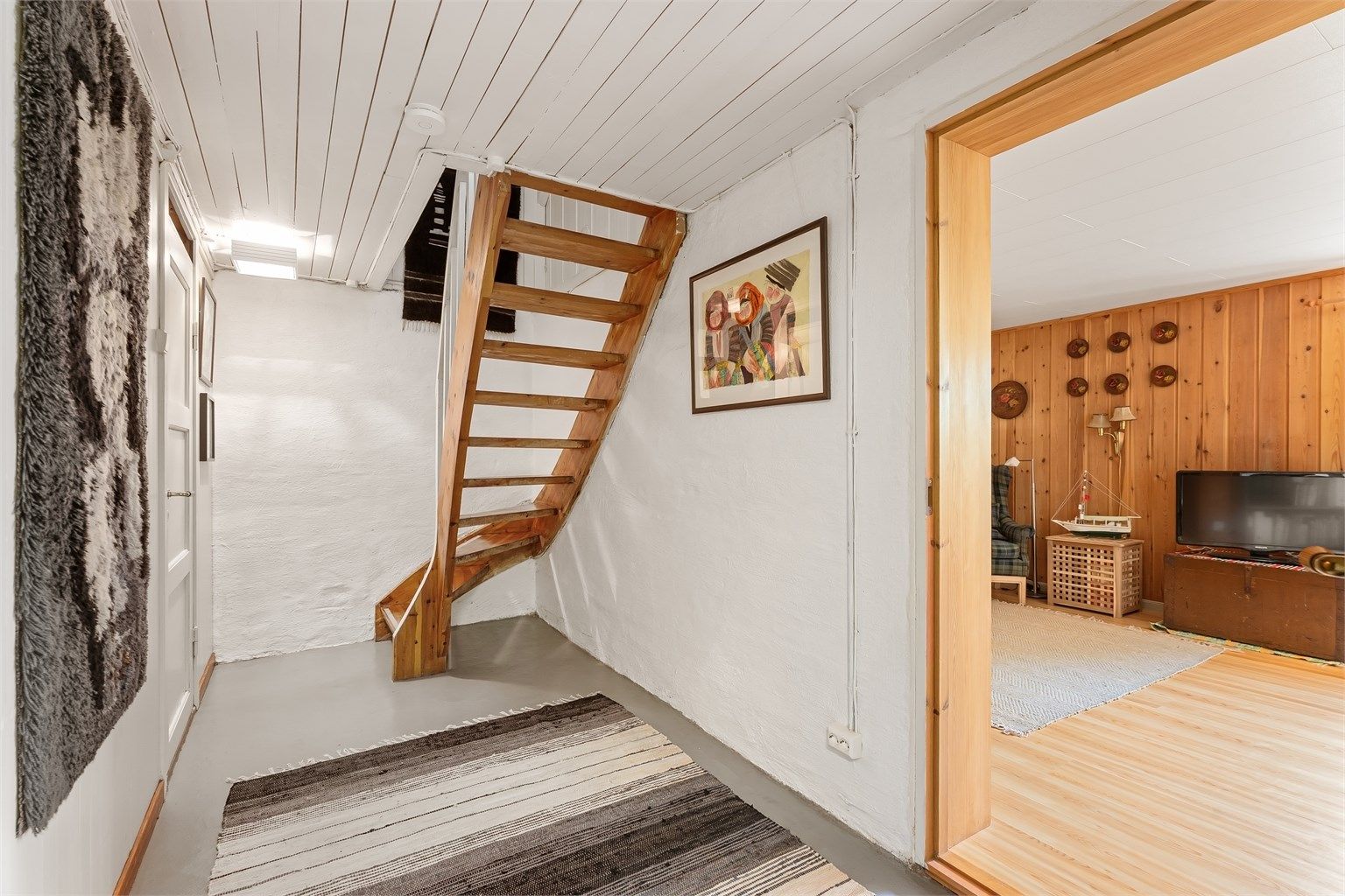 Kjellergang med malt betonggulv og adkomst til boder, vaskerom og innredet rom.