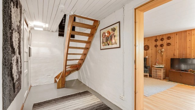 Kjellergang med malt betonggulv og adkomst til boder, vaskerom og innredet rom.
