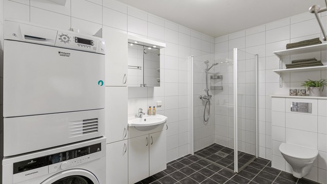 Flislagt baderom med gulvvarme, dusjhjørne og opplegg for vaskemaskin.