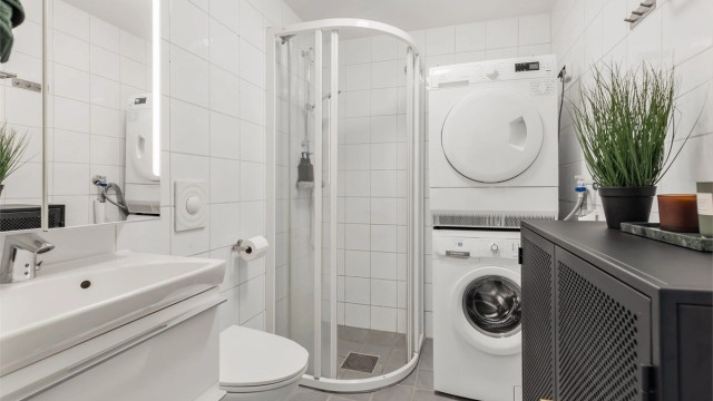 Flislagt bad med dusjhjørne som har skyvedørsramme