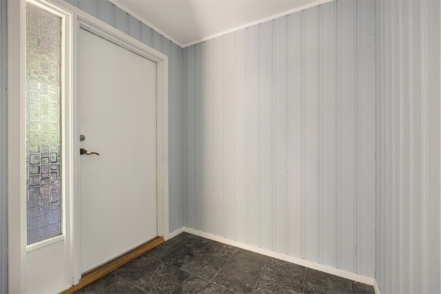 Entré med laminatgulv og malt panel på veggene.