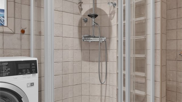 Dusjnisje med buede glassdører og regnfallsdusj.