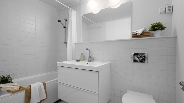 Bad I med fliser på gulv og delvis på vegg, varme i gulv.
Det er vegghengt toalett, badekar med dusj, servant med skuffer .