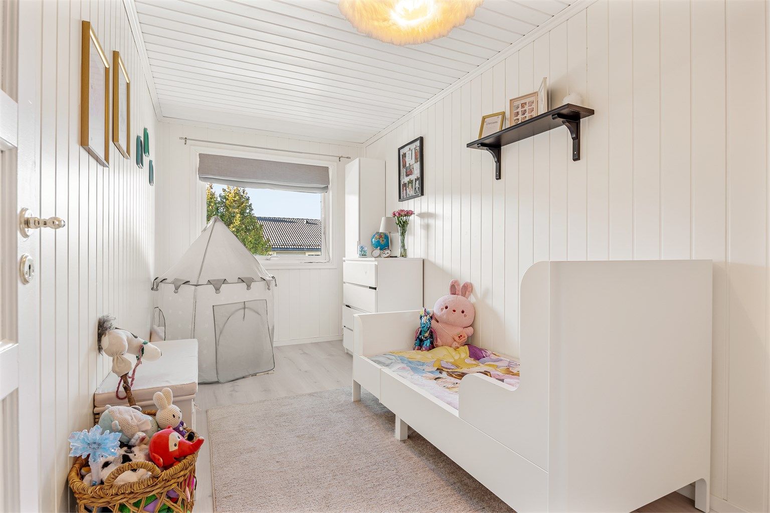 Lyst soverom innredet som barnerom med plass til seng, lekekrok og kommode.