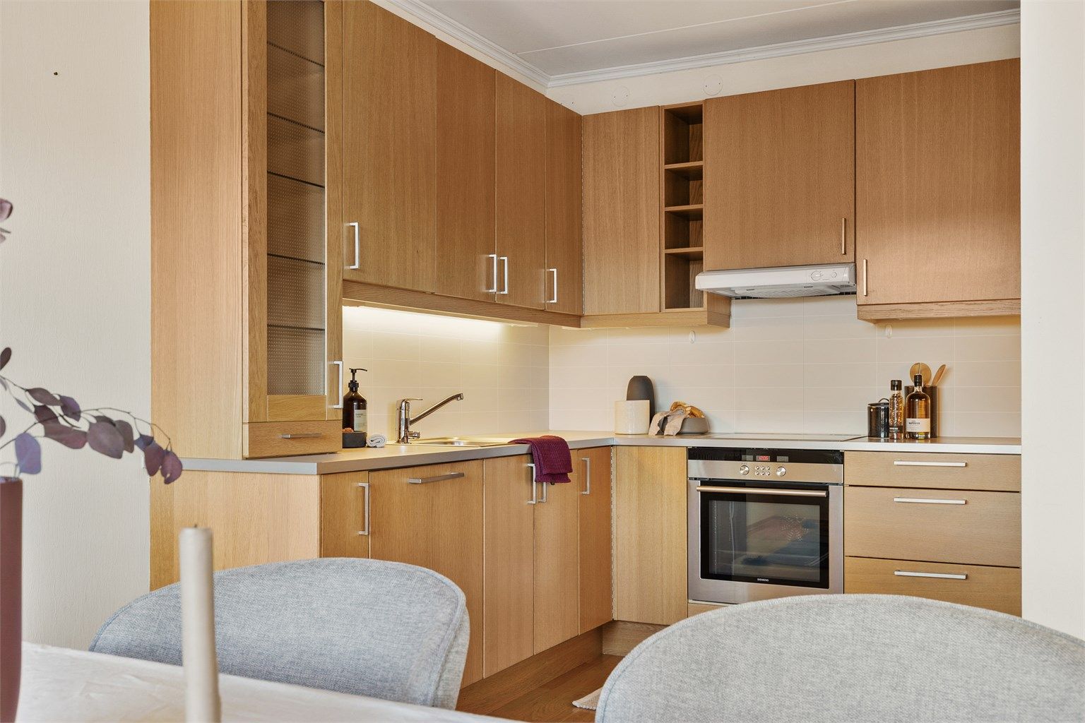 Åpen kjøkkenløsning. Innredning fra byggeår. Glatte fronter. Benkeplate med laminert overflate. Kjøkkenvask med armatur. Stikkontakt over kjøkkenbenk. Integrert stekeovn, platetopp, oppvaskmaskin og kjøleskap med fryser.