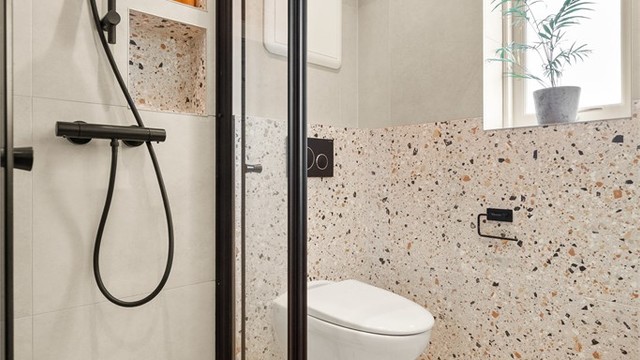 Rommet har et moderne uttrykk med flislagte gulv og vegger, gulvvarme, downlights, dusjhjørne med innfellbare dører og vegghengt toalett. Til info: Klemring i sluk er feilmontert (TG3).