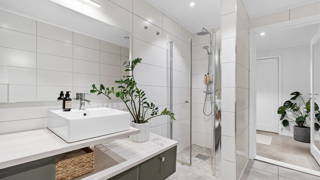 Dusjnisje med glassdør, vegghengt toalett og downlights i himling.