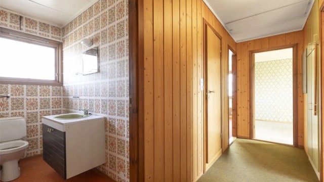 Toalettrom i hovedetasje har behov for utbedringer. Gulvbelegg på gulv, tapet på vegg og gulvstående toalett og servantskap på vegg.
