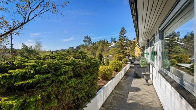 Terrassen strekker seg rundt tre sider av boligen og er omkranset av romslige blomsterkasser.