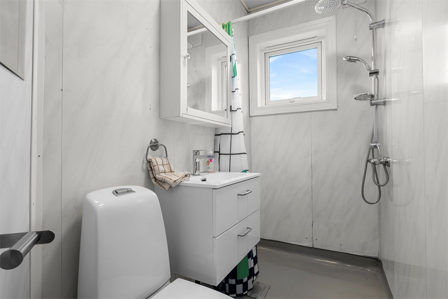 Badet har en funksjonell utforming med dusjhjørne, servant med oppbevaring og toalett.